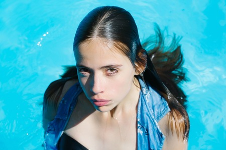 young woman or girl with pretty face and wet hair swimming in pool with blue water sunny summer day outdoorの写真素材
