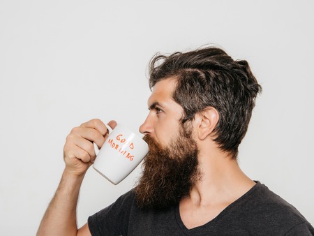 handsome bearded man with stylish hair beard and mustache on serious face in shirt holding white cup...
