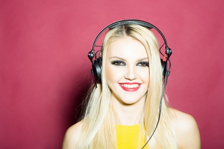 young woman or girl dj with blonde hair and red lips on pretty smiling face in yellow shirt with musical stereo headphones or headset in studio on pink backgroundの写真素材