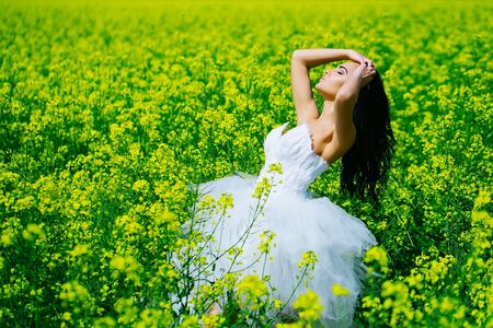 young wedding girl woman with brunette hair and pretty face in white bride dress in field with yellow green flowers on natural background sunny outdoorの写真素材