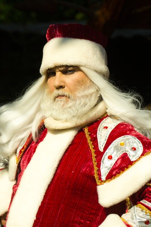 Serious santa claus man with white beard and hair in Christmas new year red suit poses in sun light outdoorsの写真素材