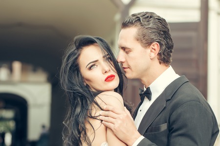 Handsome groom holds beautiful bride with passion sensual married couple outdoors on streetscapeの写真素材