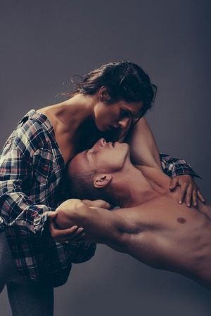 young couple of pretty slim woman with long hair in checkered shirt embracing handsome man with muscular body in studio on grey backgroundの写真素材