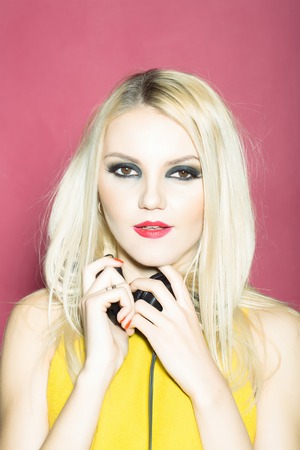young woman or girl dj with blonde hair and red lips on pretty smiling face in yellow shirt with musical stereo headphones or headset in studio on pink backgroundの写真素材