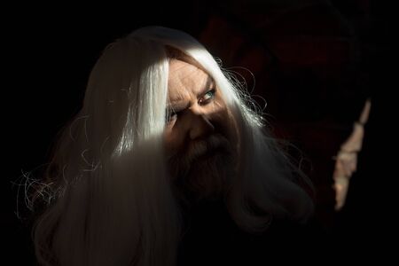 Druid old man face with wrinkles long silver beard and hair with bright light on dark backgroundの写真素材