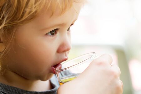 Cute baby boy blond kid with brown eyes drinks juice from glass on white backgroundの写真素材