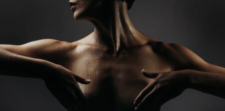young woman or girl with slim fit nude body holds hands on beautiful bare breast in studio on grey backgroundの写真素材