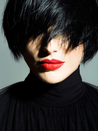 young woman or girl with short brunette stylish hair and red lips on pretty face in black cloth on grey background, closeupの写真素材