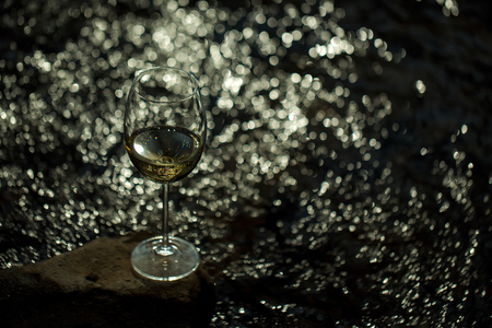 Wine glass with white wine standing on stone at seashore in sunset. Vintage lookの写真素材