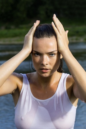 Young woman with pretty face in wet white shirt standing in sea on river water outdoor on natural backgroundの写真素材