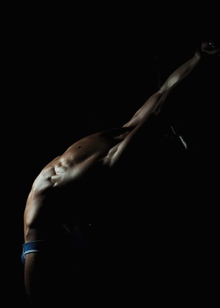 Muscular young man with athletic bare body standing on black backgroundの写真素材