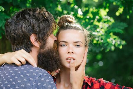 Young couple bearded handsome man hipster boyfriend hugging by hand pretty face of girlfriend on green tree backgroundの写真素材