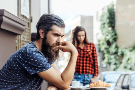 Unhappy man hipster with long beard and moustache has relationship difficulties with pretty girl in cafe outdoorsの写真素材