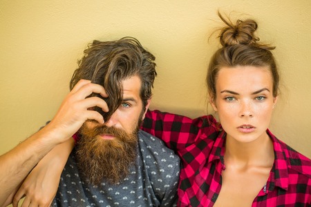 Young couple of pretty woman in checkered shirt and handsome bearded man with long beard outdoor on light backgroundの写真素材