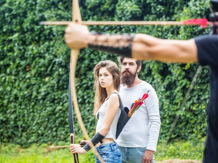 Bow shooting lesson for the attractive couple. Bearded handsome man and attractive girl learn new hobbyの写真素材
