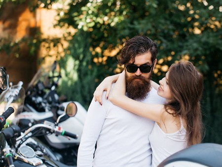 Young couple of bearded hipster man and beautiful girl hug in love outdoor near motor bikeの写真素材