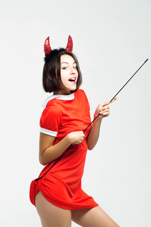 young sexy halloween woman or girl with pretty smiling face in red dress and devil horns or antlers holiday costume holds stick isolated on white backgroundの写真素材
