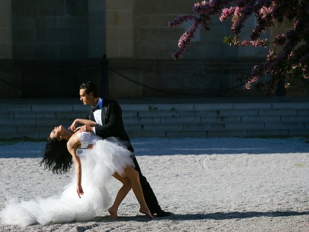 young wedding couple of sexy girl with brunette hair and pretty face in white bride dress and handsome man in black groom suit standing dancing on ground sunny outdoor, copy spaceの写真素材