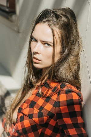 Sexy girl pretty slim model with long brunette hair in red checkered shirt sunny day outdoor on wall backgroundの写真素材