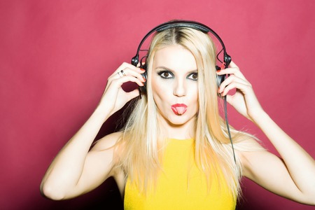 young woman or girl dj with blonde hair and red lips on pretty smiling sexy face in yellow shirt with musical stereo headphones or headset in studio on pink backgroundの写真素材