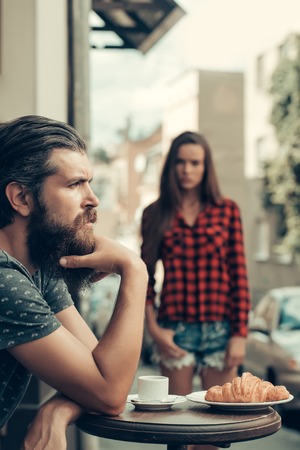 Unhappy man hipster with long beard and moustache has relationship difficulties with pretty girl in cafe outdoorsの写真素材