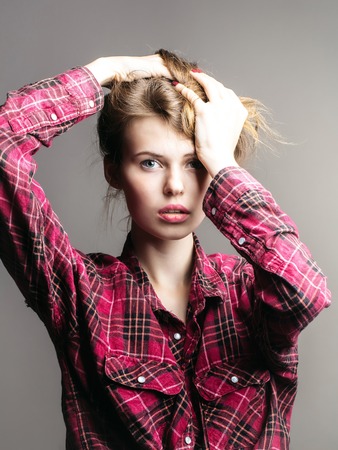 young fashionable woman or girl with long brunette hair and pretty face in stylish red checkered shirt in studio on grey backgroundの写真素材