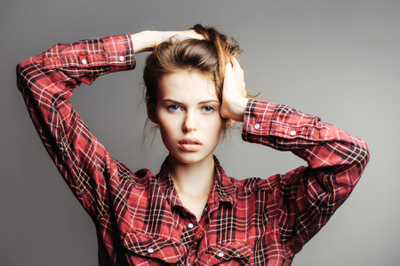 young sexy fashionable woman or girl with long brunette hair and pretty face in stylish red checkered shirt in studio on grey backgroundの写真素材