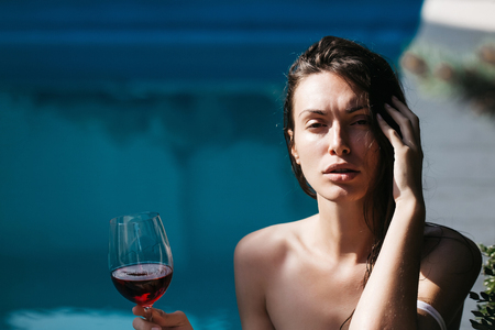 young sexy woman or girl with pretty face and long wet brunette hair drinking red wine from glass sunny day outdoorの写真素材