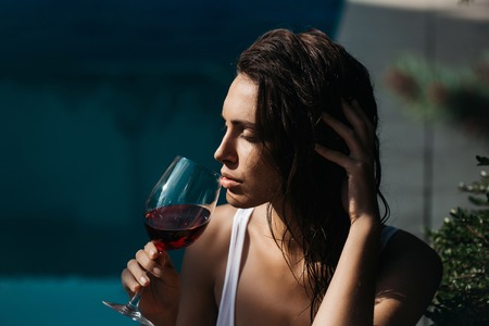 young sexy woman or girl with pretty face and long wet brunette hair drinking red wine from glass...