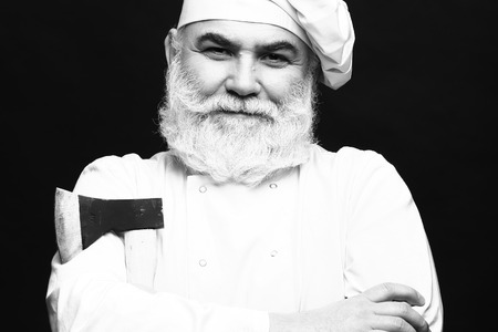 Bearded man cook in chef hat with sharp axe in studio on black background, black and whiteの写真素材
