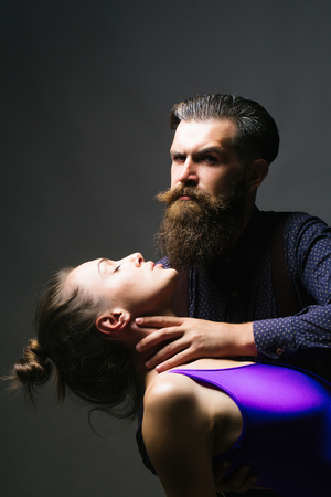Handsome man hipster with beard holds neck of beautiful young woman adult couple on grey backgroundの写真素材