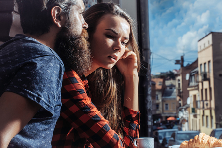 Pretty girl with long brunette hair listens to handsome man bearded hipster outdoors in street cafeの写真素材