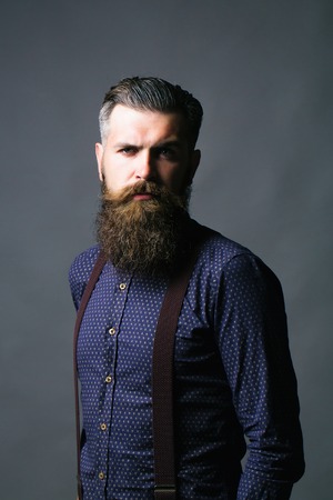 Handsome man stylish hipster with long beard and moustache in casual blue shirt with suspenders...