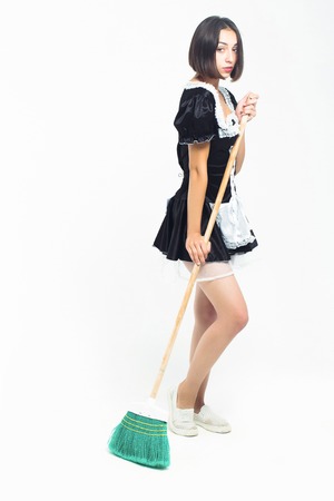 Young girl brunette with pretty face in sexy black maid costume with lace apron posing with green sweep broom isolated on white backgroundの写真素材