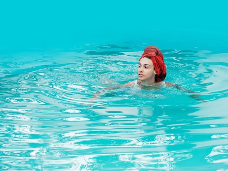 young sexy woman or girl with pretty face and terry towel on wet hair swimming in pool with blue water sunny summer day outdoorの写真素材