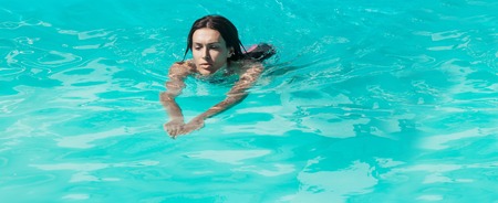 young sexy woman or girl with pretty face and wet hair swimming in pool with blue water sunny summer day outdoorの写真素材