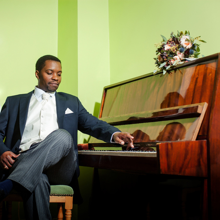 Handsome man african American groom in elegant suit with white tie and handkerchief pocket square for wedding ceremony plays pianoの写真素材