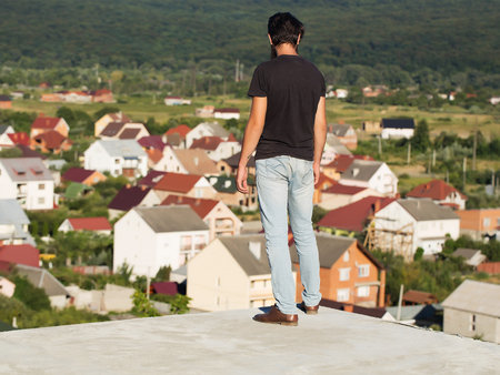 Young man brunette in black tshirt and jeans casual wear enjoys rural scenery from mountainの写真素材