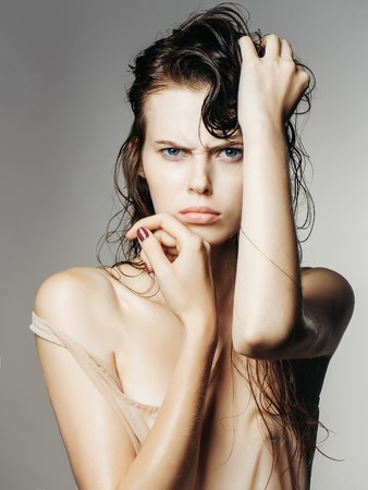 young sexy fashionable woman or girl portrait with long wet brunette hair and pretty emotional sad face in stylish beige vest in studio on grey backgroundの写真素材