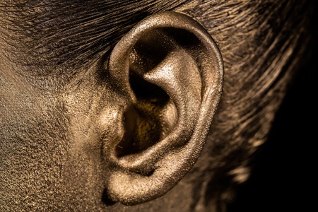 female golden or gold ear on face as makeup or body art painted metallized color, closeupの写真素材