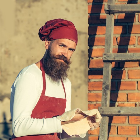 Handsome bearded man cook chef in uniform and red hat with long beard cooking in sunny day outdoor...