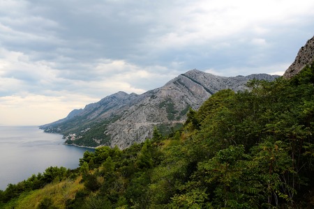 Beautiful mountain ranges coastal rock formations with high peaks cliffs and forest along sea coast on cloudy skyの写真素材