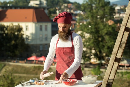 Handsome bearded man cook chef in uniform and red hat with long beard cooking in sunny day outdoor...