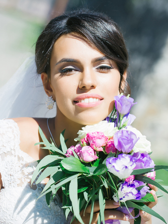 young sexy woman or girl bride with makeup on pretty face and veil in hair holding wedding bouquet or posy of eustoma and rose flowers sunny summer outdoorの写真素材