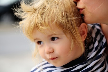 Cute baby boy child with curly blond hair and brown eyes in striped shirt outdoors on summer dayの写真素材