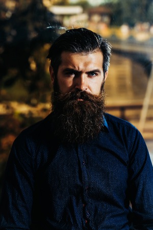 handsome bearded man with stylish hair mustache with long lush beard on serious face on city...
