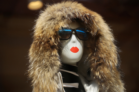 Fashion female mannequin in glamorous sunglasses and fur hood in shop on brown backgroundの写真素材