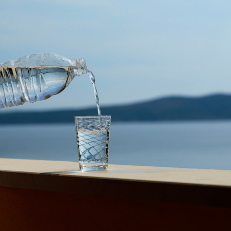 pure drinking water from plastic bottle pouring into glass outdoor on summer day on blue seaの写真素材
