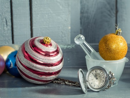 Silver clock on chain near white glass bowl and orange glitter christmas decorative balls on grey...