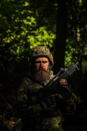 Bearded soldier in camouflage and with the gun in the forest